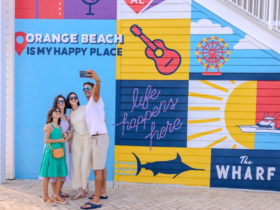 Family taking a selfie in front the mural at The Wharf entertainment district in Orange Beach